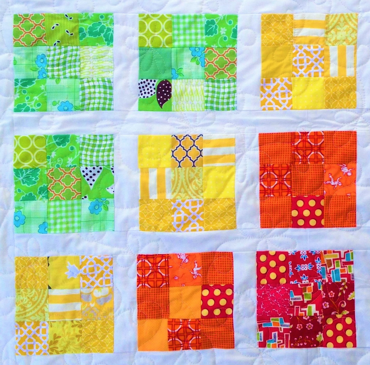 Nine patchwork quilt squares arranged in a grid, featuring various colorful fabric patterns