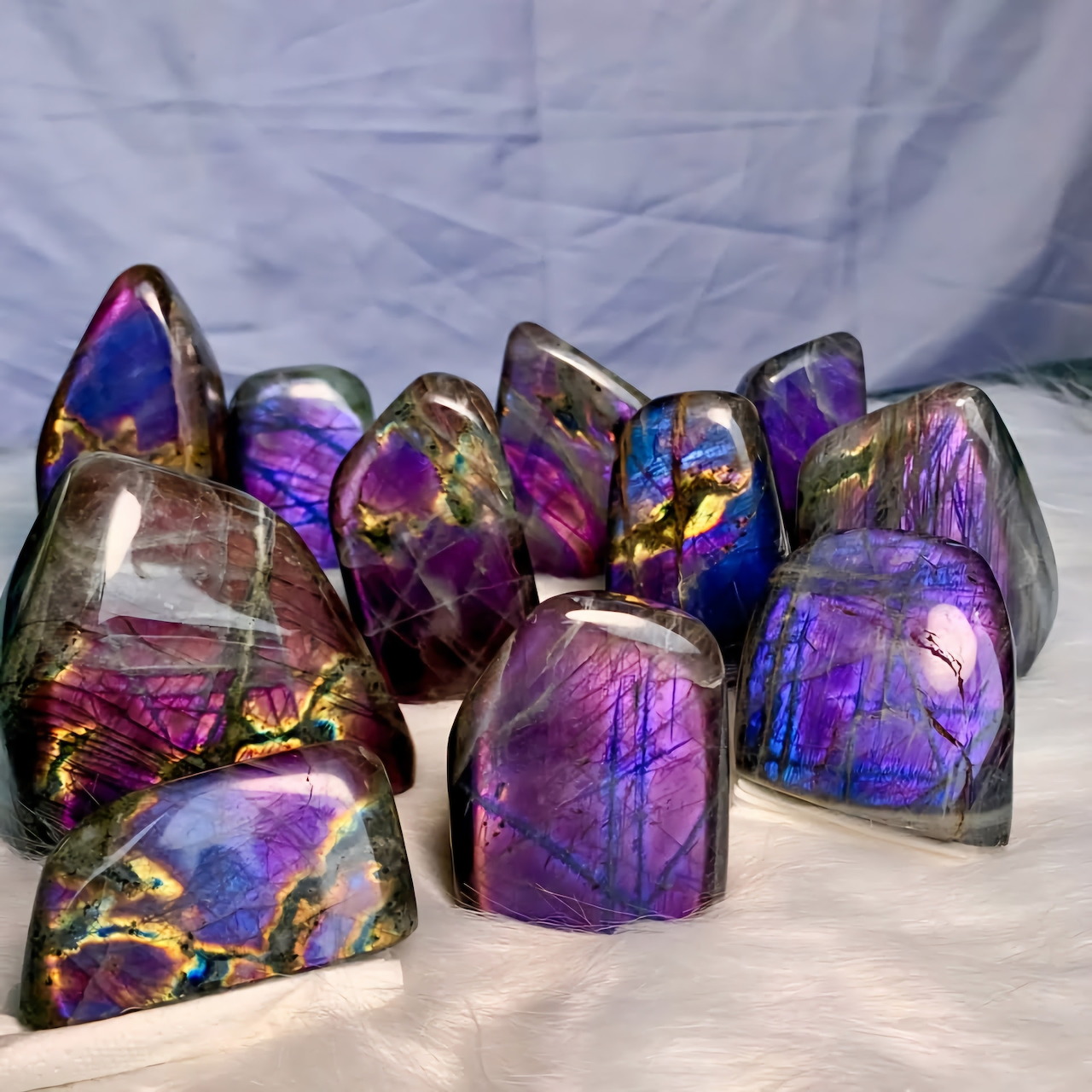 Group of polished iridescent purple and blue crystals with metallic sheen on white fabric