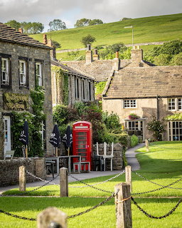 Stone cottages and red British phone box in Burnsall village with green hills behind