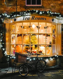 Illuminated tea room window with Christmas decorations and bicycle outside stone cottage at night