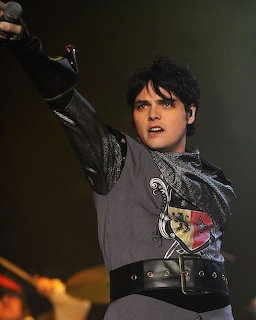 Dark-haired singer performing on stage with one arm raised and wearing a black and gray outfit