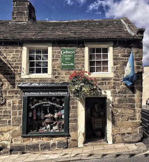 Old stone sweet shop with Cadbury's sign, hanging flower basket, and blue flag in English village