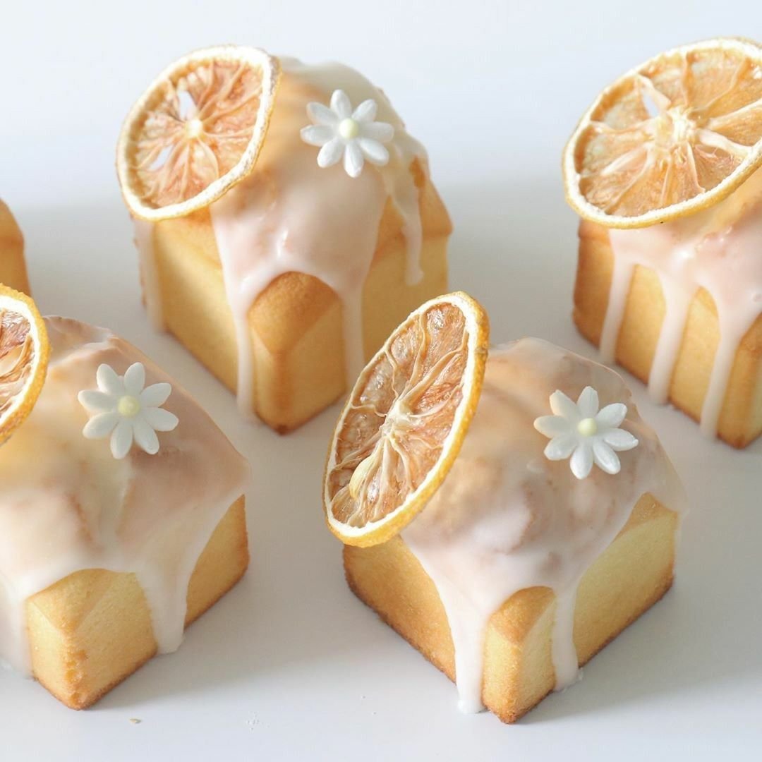 Four mini square cakes with white icing, decorated with dried lemon slices and white sugar flowers