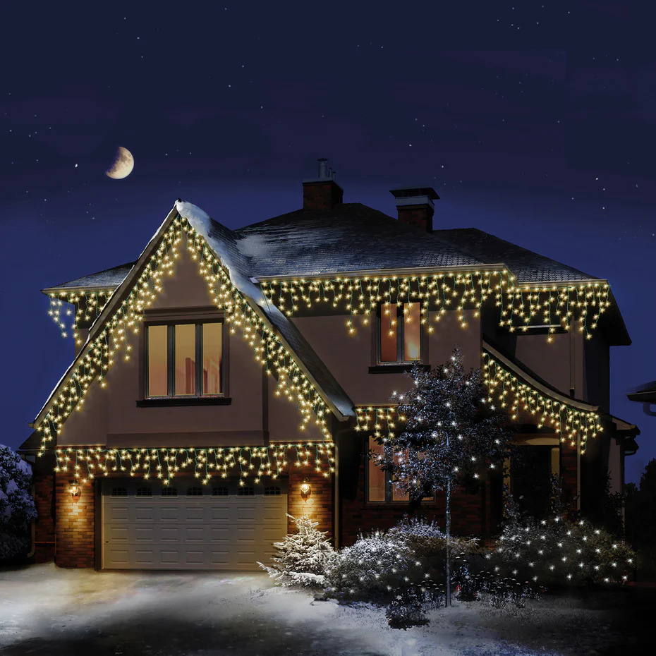 Snowy house decorated with Christmas lights at night under a crescent moon