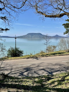 View of Lake Balaton from Fonyód with a distant hill, road in foreground, and tree branches framing the scene