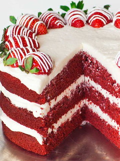 Red velvet cake with white frosting and striped strawberries, slice cut showing red and white layers