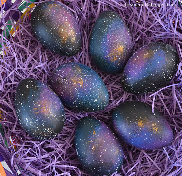Six eggs painted with dark galaxy patterns and stars in purple nest