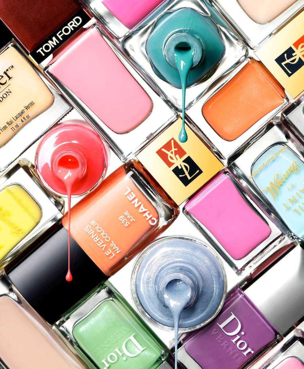 Flat-lay of multiple colorful nail polish bottles from luxury brands including Chanel, Dior, and Tom Ford
