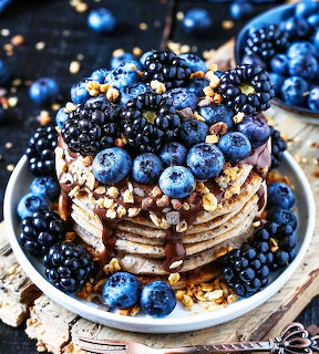 Pancake stack topped with blueberries, blackberries, granola, and syrup in a white bowl