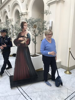 Woman standing beside a life-size cutout of a lady in a long dress inside an arched hall
