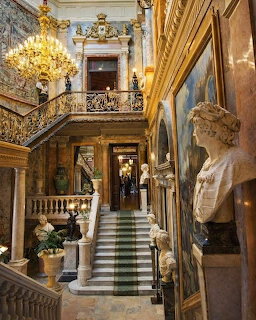 Opulent palace hall with marble staircase, gilded chandelier, classical bust and large paintings