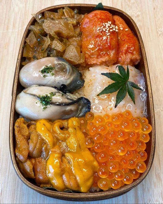 Wooden bento box with oysters, sea urchin, salmon roe, glazed meat, and a maple leaf garnish