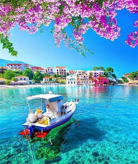 Fishing boat in turquoise Greek harbour with pink flowers and white buildings
