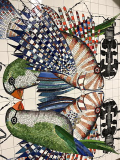 Colorful mosaic artwork of stylized birds made from small tiles on a white tiled wall