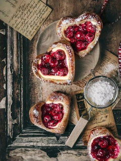 Heart-shaped cherry pastries dusted with powdered sugar on a rustic wooden tray with vintage paper