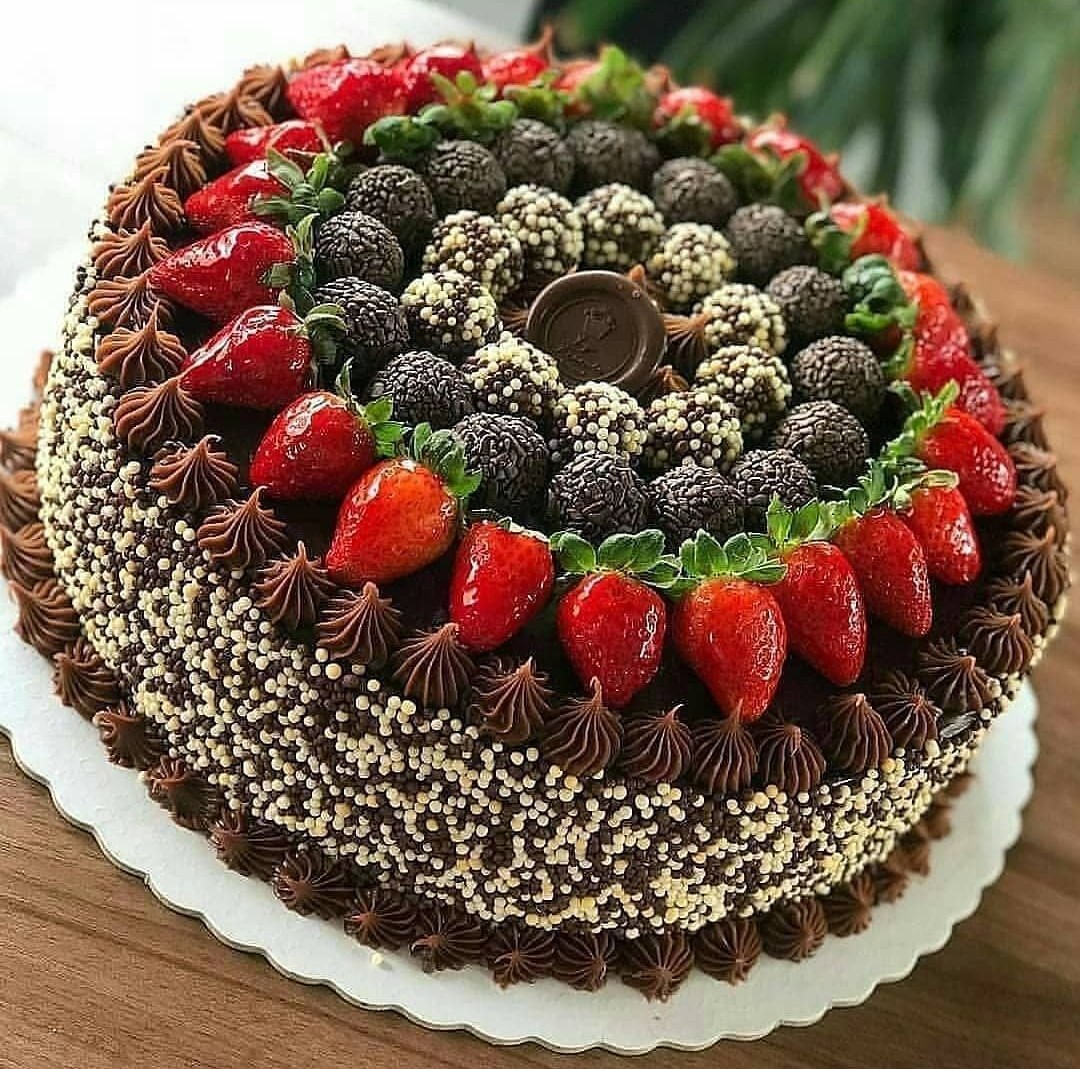 Chocolate cake topped with strawberries, dark berries, piped frosting, and white sprinkles