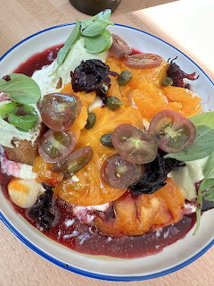 Artistic salad plate with heirloom tomatoes, greens, orange cream sauce, and dark garnishes on white dish