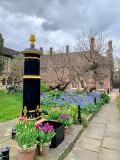 Spring flower garden at Charterhouse London with colorful blooms, black ornamental pillar, and historic brick buildings