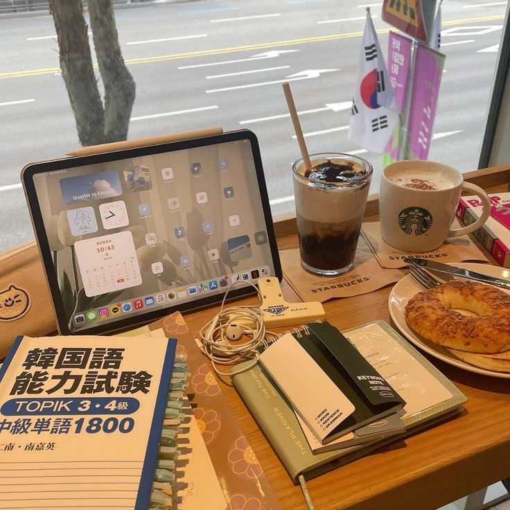 Cafe table with tablet, notebooks, coffee drinks, and a pastry by a window