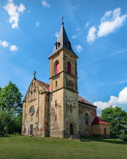 Stone church with tall bell tower and cross on green grass under blue sky