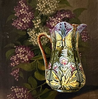 Decorative ceramic pitcher with butterfly and flower designs next to lilac blossoms