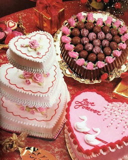 Valentine themed cakes with heart shapes, pink frosting, roses, and chocolate truffles on red tablecloth