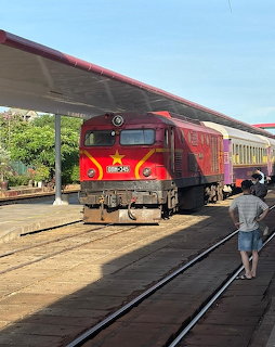 Red locomotive with yellow star at a Vietnamese train station platform with a person walking nearby