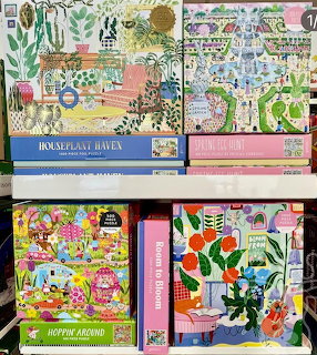 Four colorful jigsaw puzzle boxes on a retail shelf with plant and garden themed artwork