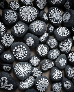 Dark pebbles painted with intricate white mandala, heart, and floral patterns arranged together