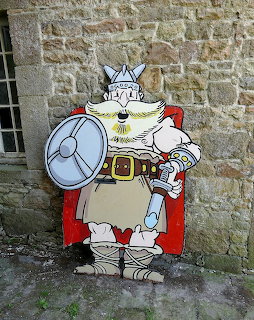 Wooden cutout of cartoon viking king with crown, shield and red cape against stone wall