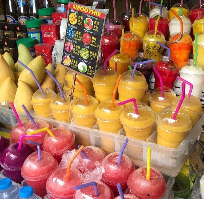 Colorful smoothies in plastic cups with straws displayed at a market stall