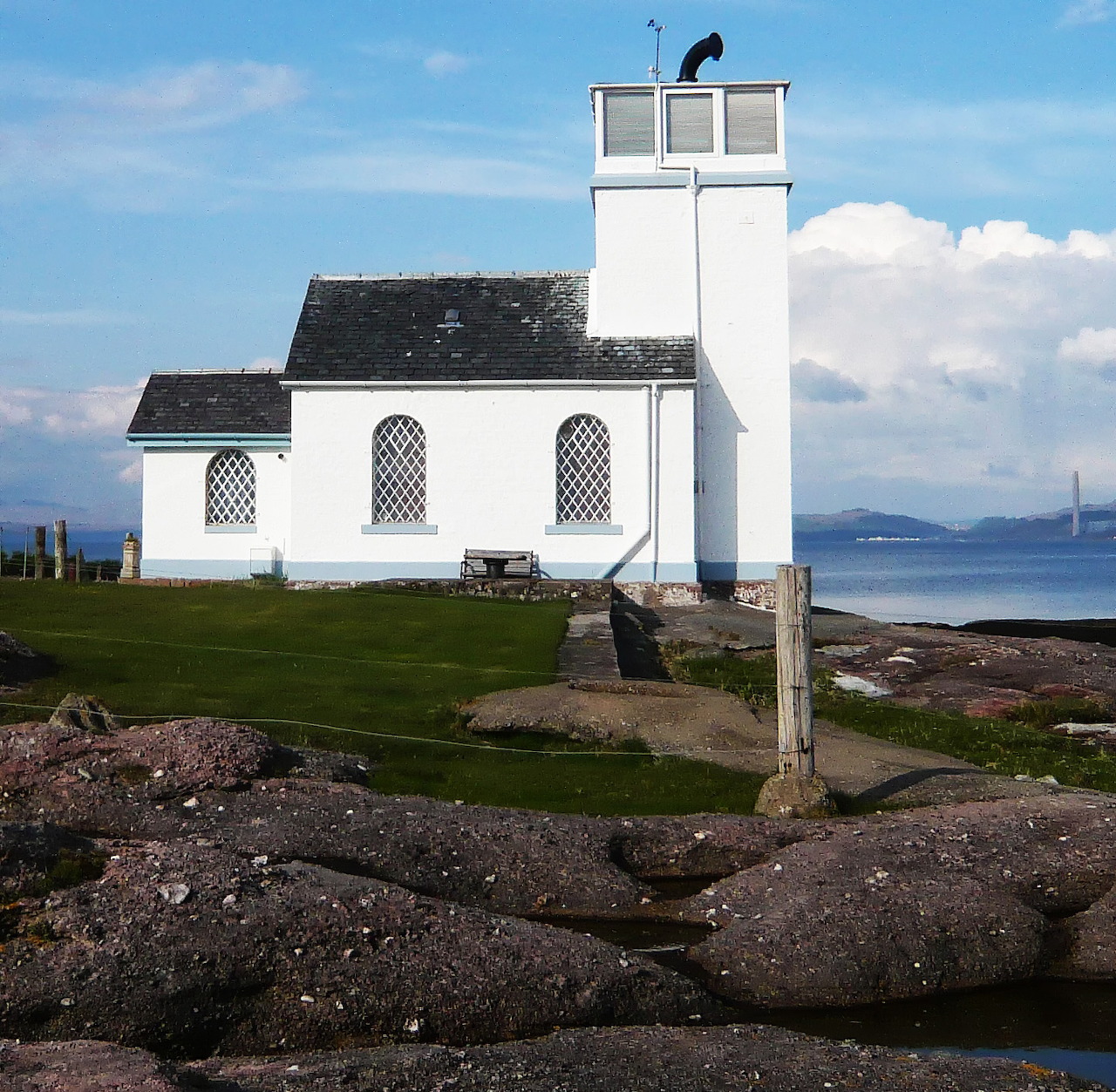 White Toward Point foghorn building on a rocky shoreline beside calm sea under a blue sky