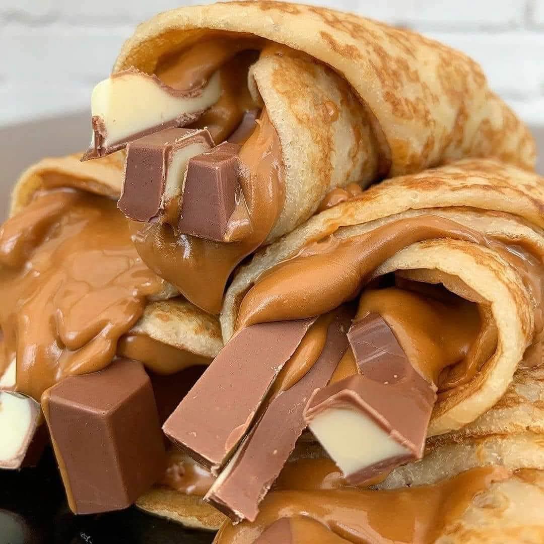 Stack of rolled crepes filled with chocolate pieces on dark plate