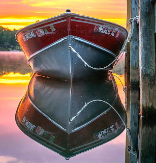 Red boat tied to wooden post with mirror reflection in calm water at sunset