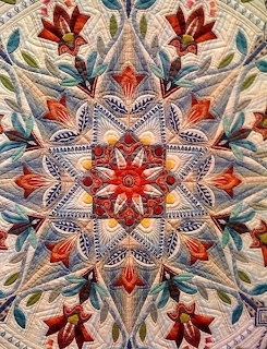 Symmetrical quilt with orange stars, blue paisley, and beige floral pattern in radial design