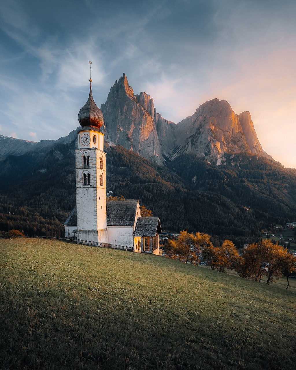 Small church in a green valley surrounded by tall mountains under a clear sky