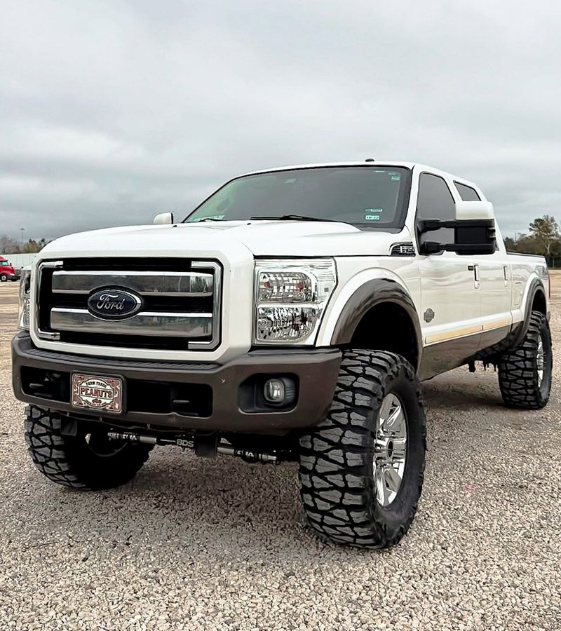 Lifted white Ford F-250 Super Duty truck with large off-road tires and chrome rims on a parking lot
