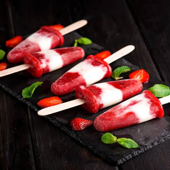Three strawberry cream popsicles with fresh strawberries and mint on dark slate