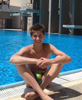 Smiling boy in swim trunks sitting by a swimming pool