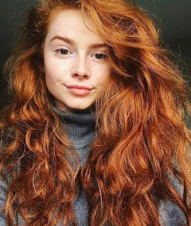 Portrait of a young woman with long red curly hair in a gray turtleneck sweater