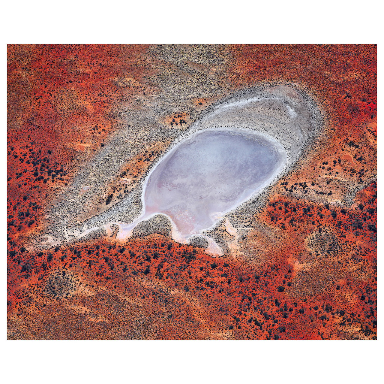 Aerial view of a pale salt lake surrounded by red and orange desert terrain