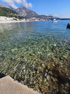 Clear turquoise water over rocky seabed with mountains and a coastal town in Montenegro