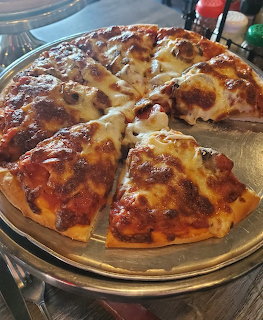 Sliced pizza with melted cheese and toppings on a round metallic plate