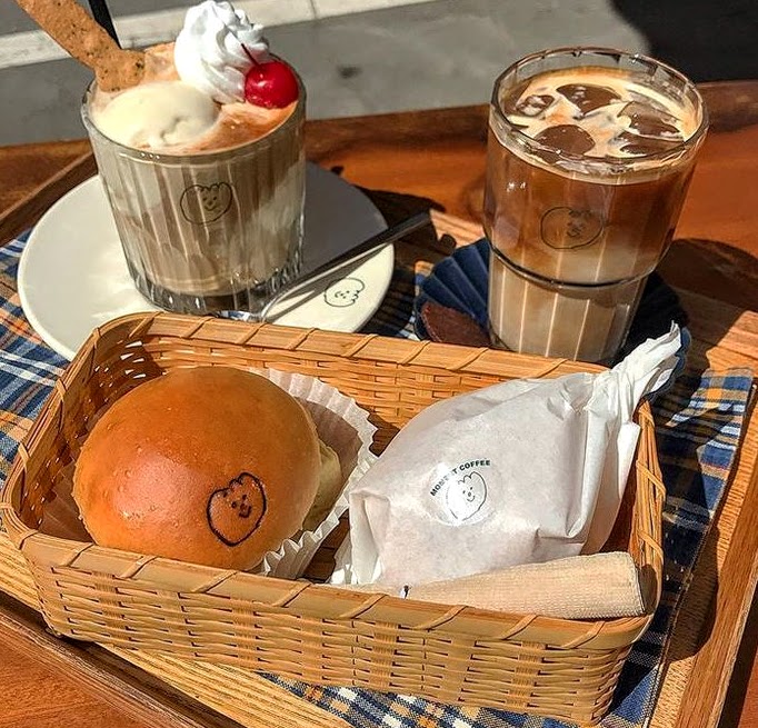 Basket with a bun and wrapped pastry next to two iced coffee drinks on an outdoor table