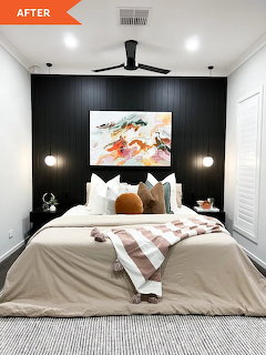 Modern bedroom interior with black accent wall behind bed, white and orange bedding, abstract art, ceiling fan