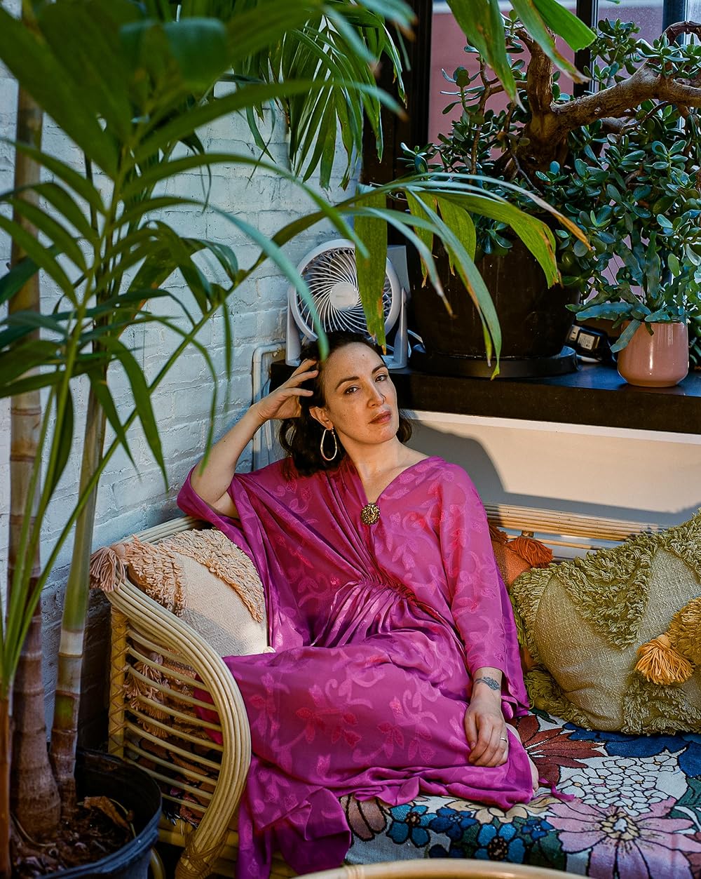 Woman in pink satin dress sitting on rattan chair surrounded by tropical houseplants