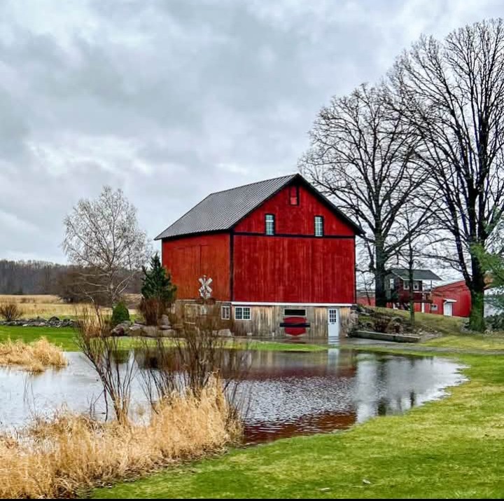 Red barn beside lake with bare trees and cloudy sky in rural landscape