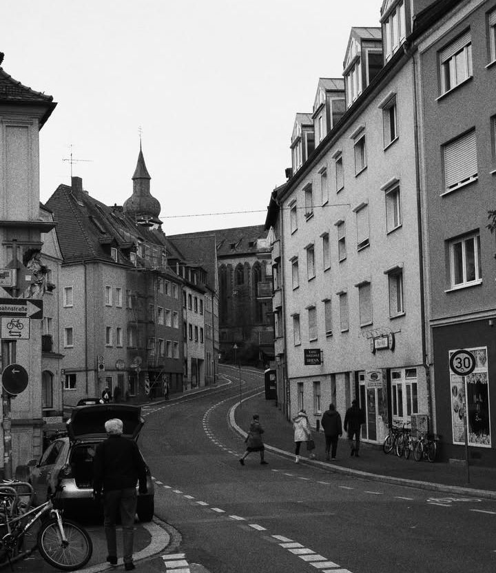 Black and white photo of a winding European street with old buildings and a church steeple in the background