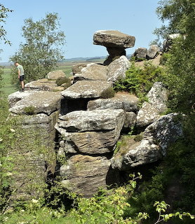 Weathered sandstone rock formations at Brimham Rocks with balancing stone and green surroundings