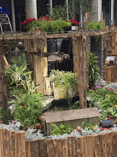 Rustic wooden garden display with waterfall, ferns, and lush green plants indoors